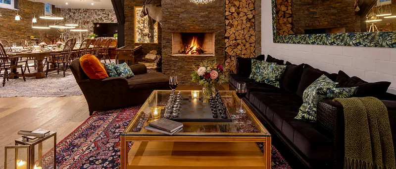 Die Kaminlounge mit brennendem Feuer, Holzstapel und tiefen Sofas
